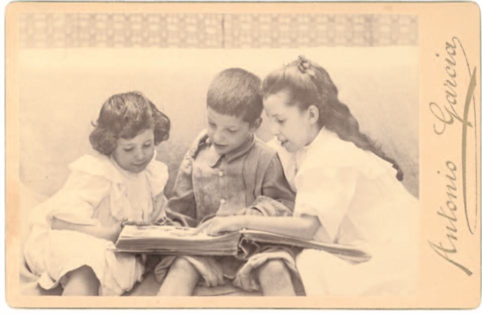 # 81.- García Peris, Antonio Elena, Joaquín y María Sorolla García, 1901 (ca.) Albúmina. 98 x 139 mm. Positivo antiguo Carta fotográfica: 165 x 105 mm. Cabinet Antonio García impreso en dorado (lateral derecho del anverso de la carta fotográfica); Luz y / Arte / Fotografía / Anto. García / Valencia / Plaza de Sn. Francisco N.º 10 / Prager & Lojda. Berlín impreso en marrón (reverso de la carta fotográfica) N.º Inv. 80243 Retrato de estudio de los tres hijos del artista observando un álbum fotográfico, foto extraida del catálogo LA COLECCIÓN DE FOTOGRAFÍA ANTIGUA DEL MUSEO SOROLLA